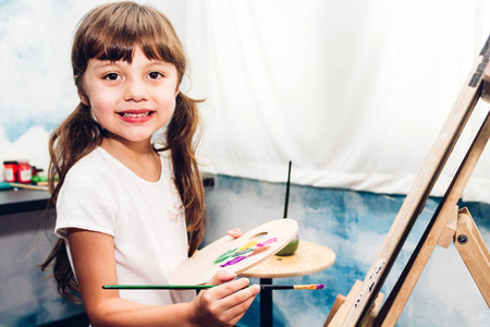 小女孩艺术家在画布上绘画与调色板和水彩颜料在家里