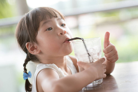 小亚洲小孩喝冰巧克力, 在咖啡馆里给拇指吃。自然光户外生活方式