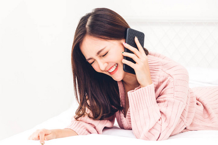 快乐的女人放松使用和交谈的智能手机在家里的床上. 技术与沟通理念
