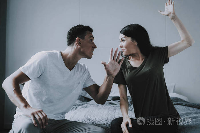 女人和男人在家里坐在床上打架.已婚夫妇坐在灰色格子和争吵.