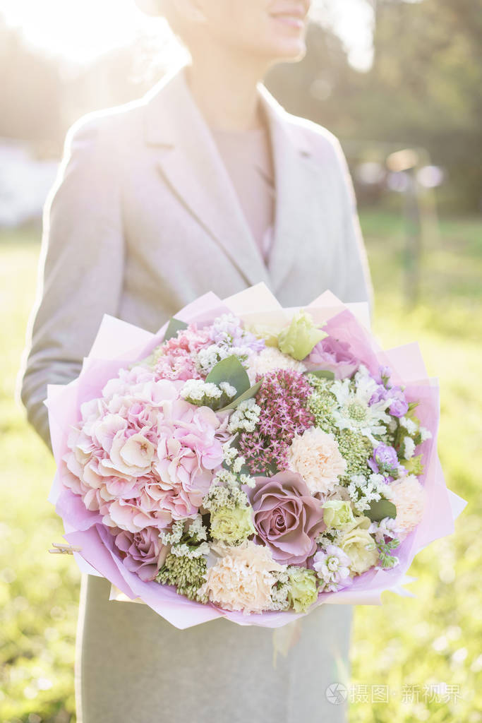 年轻女孩捧着一束美丽的春天花束插花与花绣球和花园