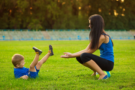母亲和小儿子在夏季公园草地上玩球