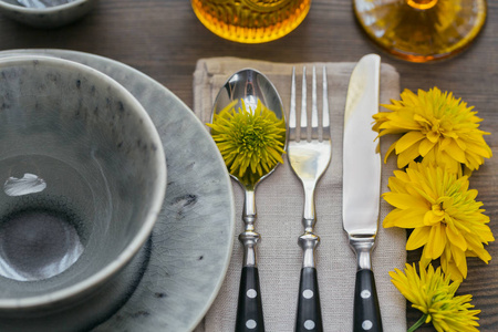 质朴的餐桌设置, 亚麻餐巾, 餐具, 陶瓷板, 黄色眼镜和黄色的花朵在黑暗的木桌上。节日餐桌装饰。浪漫晚餐