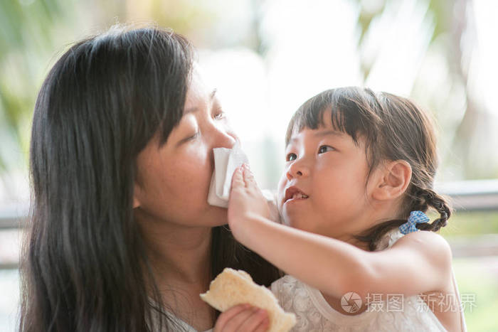 孩子帮助妈妈在咖啡馆擦嘴。亚洲家庭户外生活方式与自然光