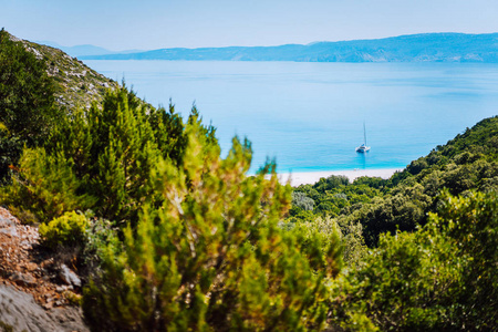 孤独的游艇上隐藏 Fteri 海滩泻湖, 凯法利尼亚, 希腊。松树树枝之间的框状视图徒步下山的小路