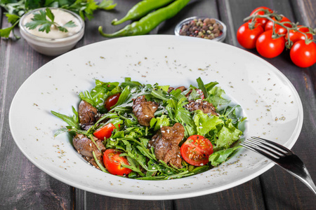 热沙拉与油炸肝, 樱桃西红柿和混合蔬菜在黑暗的木质背景。健康食品。餐桌上的配料。顶部视图