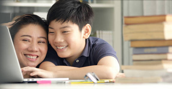 可爱的亚洲母亲帮助您的儿子在家做家庭作业与微笑面孔一起