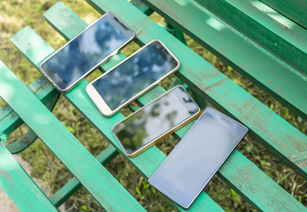 四个现代智能手机在夏天的长凳上