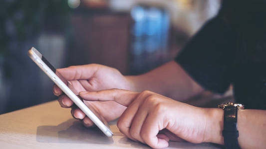 在现代咖啡馆里手持使用和指着智能手机的妇女