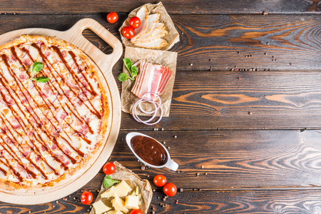 食品背景设计。培根, 洋葱, 奶酪, 红色烧烤酱在一个黑暗的木制背景。披萨食材