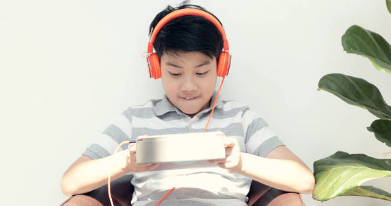 可爱的亚洲男孩观看和玩平板电脑与快乐的脸