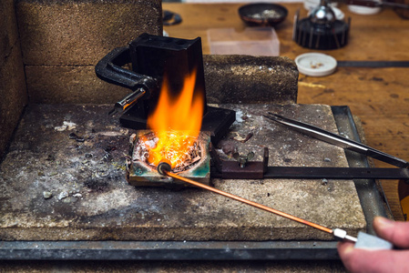 黄铜金属与火炬火焰熔化在一个坩埚在工作地点的金匠为执行工艺品金属制品