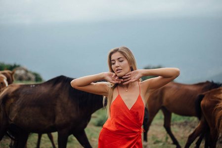 可爱的女孩在红色礼服摆在自然背景。板栗马在她身后奔跑。把手放在脸附近