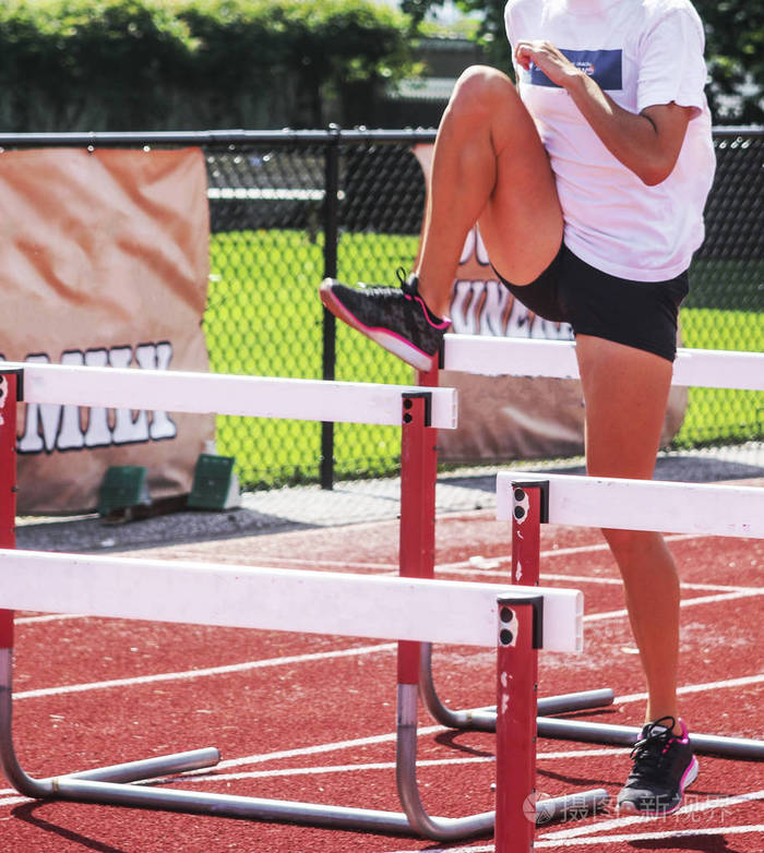 一名女跨栏运动员正在田径练习中, 在跨栏的一侧进行一次跳过的训练