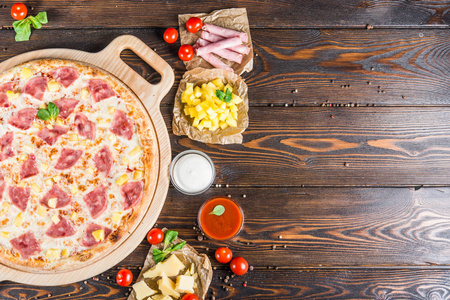 大比萨饼与火腿和菠萝在一个圆形的切菜板上的一个黑暗的木制背景。食品配料