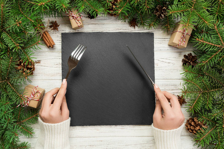 顶视图女孩手里拿着叉子和刀, 准备吃饭。空黑色石板方板在木圣诞节背景。节日晚餐菜的概念与新年装饰