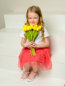 一个小女孩带着一束郁金香坐在楼梯上