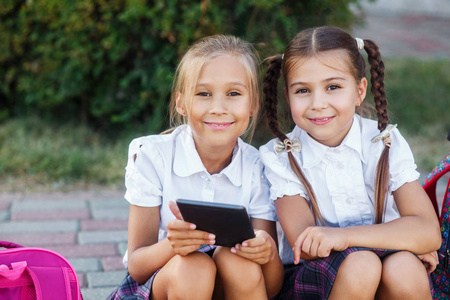 年轻女孩读电子书.小学生的小学.女孩与背包附近建筑户外照片