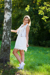 年轻美丽的金发女郎夏天白色礼服在夏天绿色公园背景
