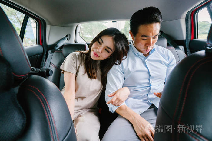 两位年轻的亚洲商人坐在一辆汽车的后座上, 开车到他们的目的地, 乘坐