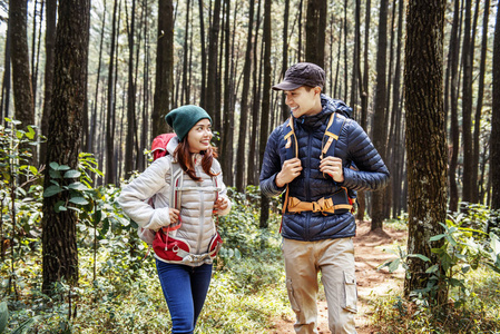 年轻的亚洲夫妇徒步旅行者与背包走在森林小径上