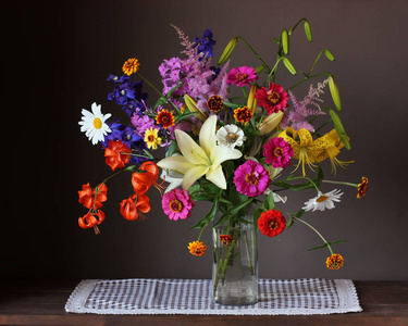美丽的鲜花花束在一个玻璃花瓶在黑暗的背景。百合和百日草