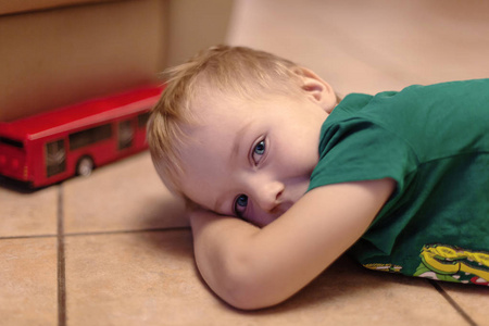 可爱的小男孩与蓝色的眼睛躺在陶瓷地板上的玩具 红色巴士。金发, 绿色 t恤。室内
