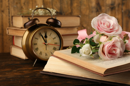 鲜花和时钟木制背景上的书