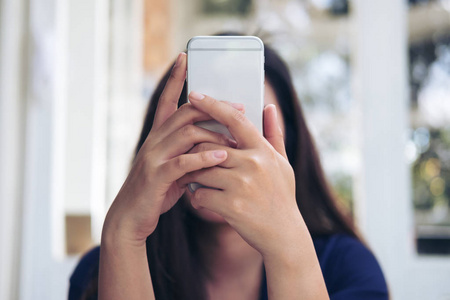 一个亚洲妇女手持, 使用和看智能手机遮住她的脸在咖啡馆