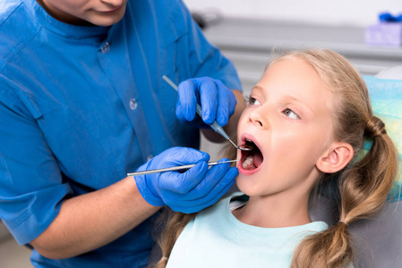 裁剪拍摄的牙医与工具检查牙齿的小孩