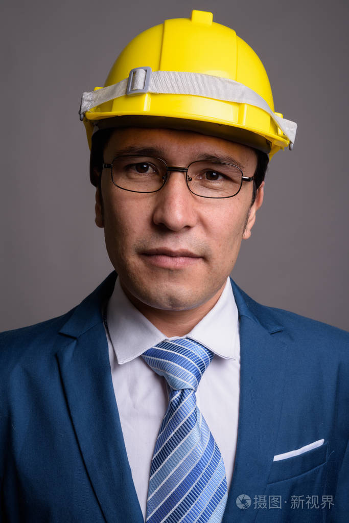 年轻的亚洲商人在灰色背景下戴安全帽