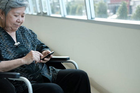 坐在轮椅上的老妇人手持手机。老年女性短信信息, 使用智能手机在家里的应用