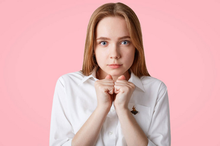 画像认真聚焦可爱的女人紧握拳头, 穿白衬衣, 有希望的东西, 与世隔绝