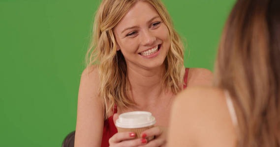 漂亮的金发碧眼的女性在绿色屏幕上与女性朋友在咖啡上交谈