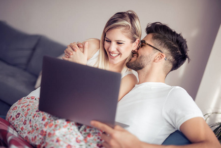 愉快的夫妇一起放松在沙发和使用膝上型电脑在家庭在客厅里