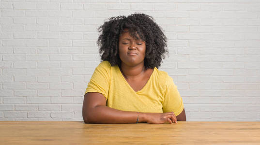 年轻的非洲裔美国妇女坐在家里的桌子上与手上的胃因为消化不良, 痛苦的疾病感到不适。疼痛概念
