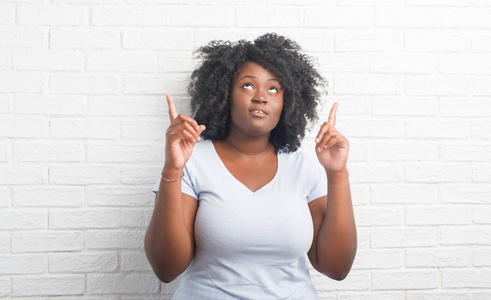 年轻的非洲裔美国人加上大小的女人在白色砖墙惊讶和惊讶地看着手指和举起手臂