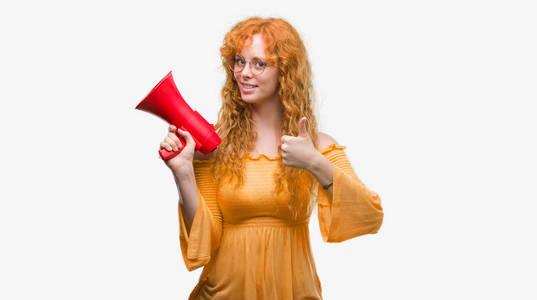 年轻红头发的女人拿着扩音器高兴与大微笑做 ok 标志, 拇指与手指, 优秀的标志