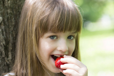 美丽的小女孩吃一个多汁的新鲜草莓