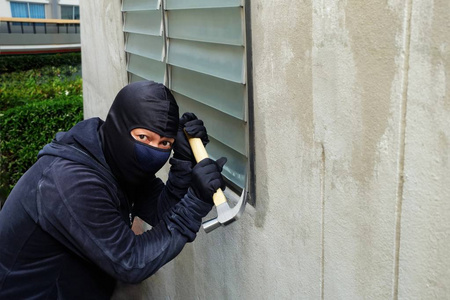 蒙面小偷用锤子试图打破窗户和震惊的脸表情照片