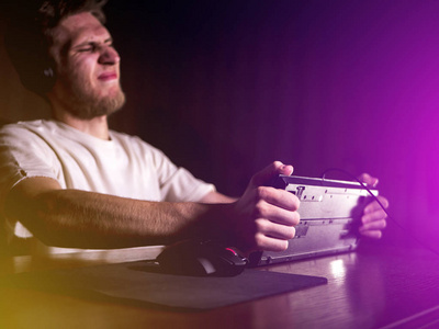 年轻疯狂疯狂的玩家打破键盘玩电脑游戏在计算机上深夜