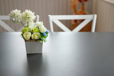 黑色桌子上的人造黄色玫瑰。白色椅套在舒适的餐厅内饰