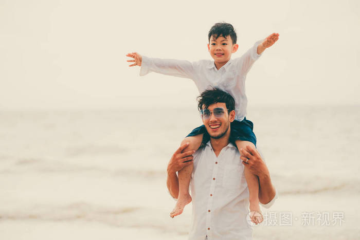 快乐的父亲在夏天的热带沙滩上背着儿子的脖子上