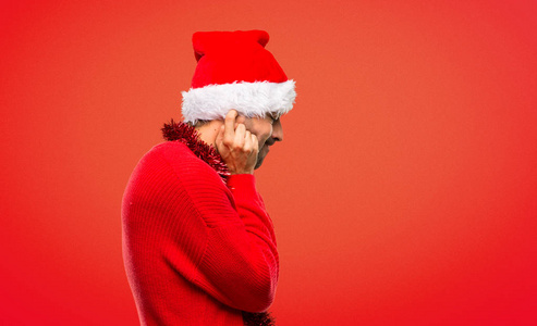 着红色衣服庆祝圣诞节假期的男子用双手在红色背景上捂住两只耳朵照片