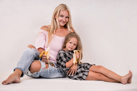可爱的紧密针织家庭的妈妈和女儿坐在白色背景上吃香蕉