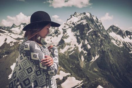 波西米亚的女人戴着帽子和斗篷站在山边。寒冷的天气, 山上的雪。冬季远足。流浪