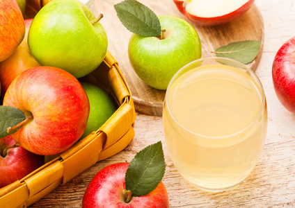 一杯新鲜的有机苹果汁与红色和绿色的苹果在木材背景的老式篮子