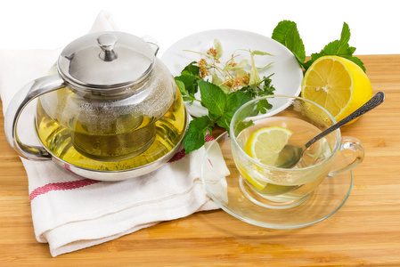 玻璃茶壶中的草药茶, 有过滤器, 玻璃杯, 柠檬和草药, 用于在木质表面上的茶托上制作茶叶。