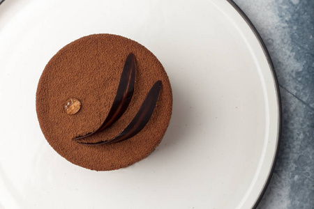 巧克力蛋糕放在盘子上, 用一滴露水和巧克力叶子缠结在一起。在光的背景下。从上面查看