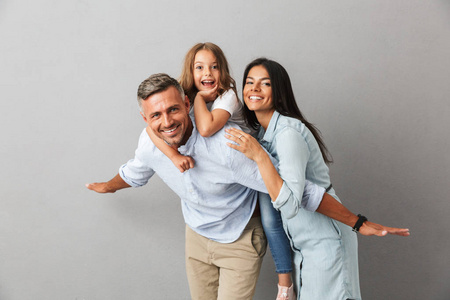 一个开朗的家庭父亲, 母亲, 小女儿一起玩的肖像, 父亲抱着小女儿在他的背部孤立的灰色背景